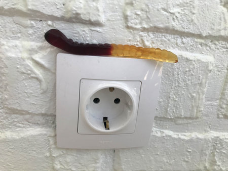 gummy worm on the background of a white brick plastered wall. a gelatinous worm lies on a white...
