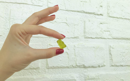 a gummy yellow bear in the hands of a girl with a red manicure. teddy bear is held in hand against...