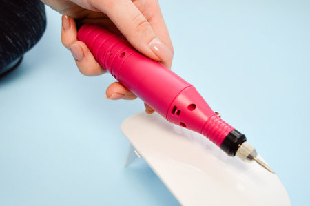 The process of making a beautiful manicure on the hands on the fingers with the help of a special machine and a lamp for drying the varnish in the nail beauty salon on a blue background.の写真素材