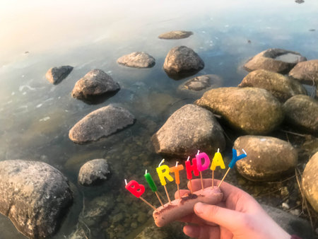Happy birthday inscription made of holiday candles in the hands of a man and a woman opposite the...