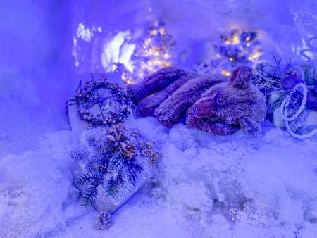 Festive design scene: a toy bear sleeps in a snow-covered den, a decorated tree behind him.