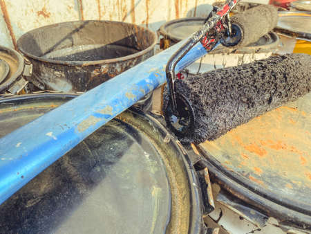 construction site. on the ground are barrels of paint and resin. black resin is spilled from the barrel. on the barrels lies a blue heavy beam and a paint roller.の写真素材