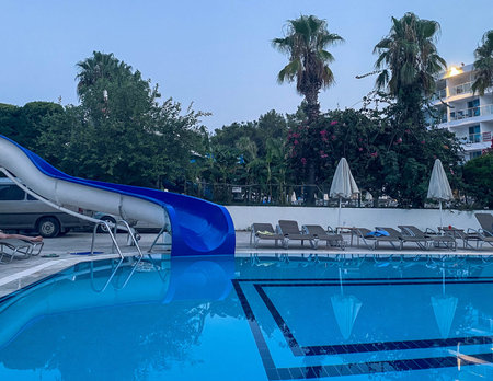 rest of tourists by the pool with chlorinated, turquoise water. water park on site, blue slides to...