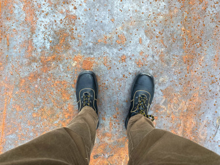 Legs of a man in boots on the background of a rusty old iron red scratched metal corrosed sheet...