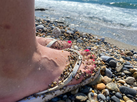 Female legs, feet in rubber slippers with a beautiful red pedicure on the background of sand on vacation on the beach in a warm tropical eastern paradise country southern resort.の写真素材