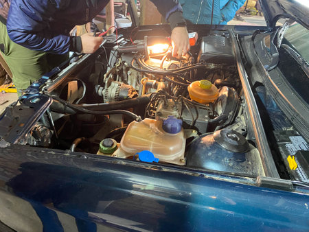 Working master locksmith repairman repairs a car under the hood in a workshop in a garage.の写真素材