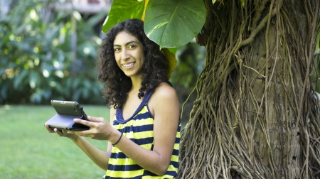 Teenage girl leaning against a tree using a tablet.の写真素材