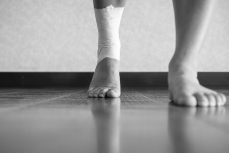 Black and white version of Athlete walking forward with an ankle injury and ankle tape jobの写真素材