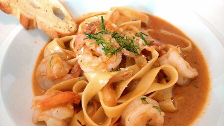 Prawn pasta with sauce on a white plate on a white backgroundの写真素材