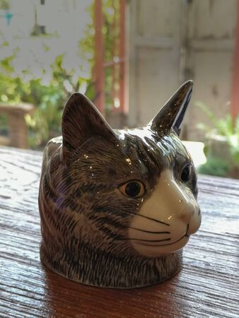 The gray cat's head is ceramics placed on a wooden table, the background is blurred.の写真素材