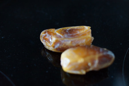 A handful of dates with warm hues rests gently on a natural surface, revealing their deep glow and...