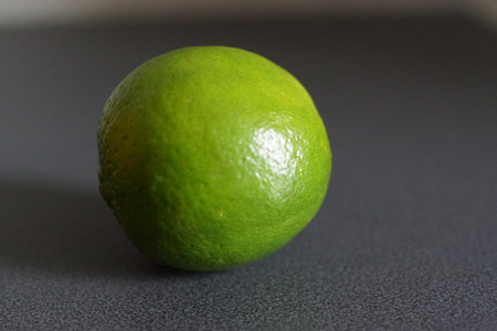 A lime sits elegantly on a smooth surface, bathed in natural light that enhances the intensity of its color.の写真素材