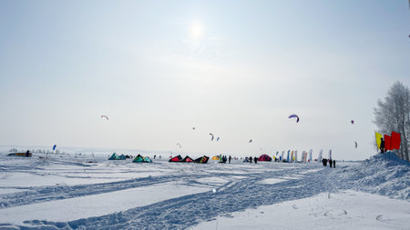 A lot of people are engaged in snowkiting in a snowy area, surrounded by tents.の写真素材