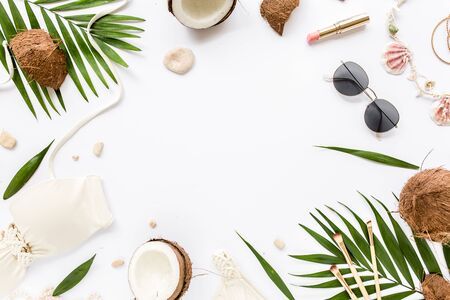 Feminine beige swimsuit beach accessories, tropical palm leaf branches, coconuts on white background. Summer background. Road frame set.の写真素材
