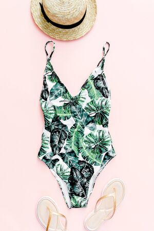 Woman's beach accessories: swimsuit with tropical print, straw hat on pink background. Summer background. Flat lay, top view.の写真素材