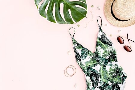 Womans beach accessories: swimsuit with tropical print, straw hat on pink background. Summer background. Flat layの写真素材