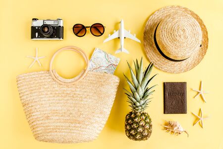 Womans beach accessories: rattan bag, straw hat, retro camera, model plane, airplane on yellow background. The concept of travel. Summer background.の写真素材