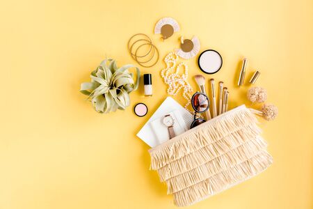 Woman straw bag with travel accessories, makeup brushes, cosmetics, golden accessories on yellow background.の写真素材