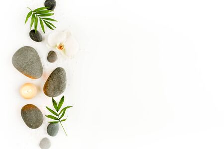 Spa stones, palm leaves, flower white orchid, candle and zen like grey stones on white background. Flat lay, top view. High quality photoの写真素材