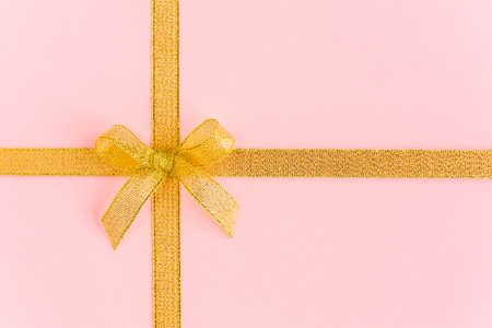 Gold ribbon with bow, isolated on pink background. Colorful celebration, birthday background. Flat lay, top viewの写真素材