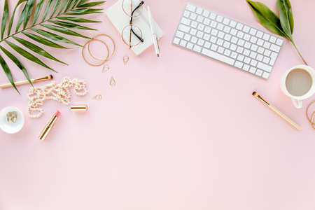 Office table desk with computer, green leaves palm, clipboard. Top view. Flat lay. Home office workspace. Womens accessories on pink background.の写真素材
