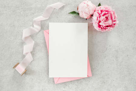 Mockup invitation, blank paper greeting card, pink envelope and peonies on gray stone table. Flower background. Flat lay, top view.の写真素材