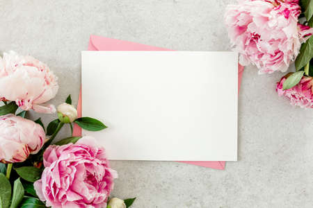 Mockup invitation, blank paper greeting card, pink envelope and peonies on gray stone table. Flower background. Flat lay, top view.の写真素材