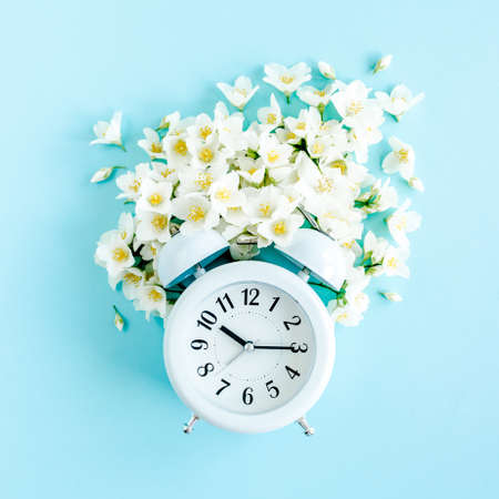 Composition-Summer time from Jasmine flower and clock, alarm on blue background. Flat lay, top view