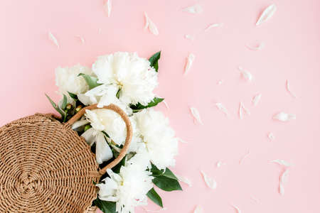 White bouquet of peonies in a straw bag on pink background. Minimal floral concept greeting card. Flat lay, top view.