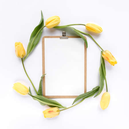Clipboard mock up with beautiful yellow tulips isolated on white background. Flat lay, top view....