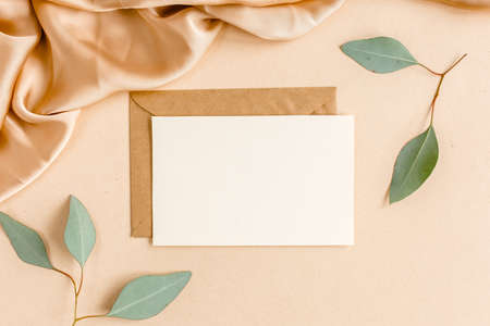 Mockup invitation, blank greeting card and craft envelope, green leaves eucalyptus. Flat lay, top...