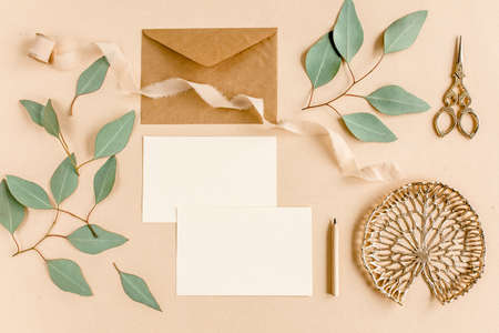 Mockup wedding invitation, blank greeting card and craft envelope, green leaves eucalyptus. Flat lay, top view.の写真素材
