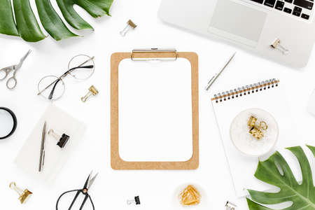 Home office workspace mockup with laptop, tropical leaves Monstera, clipboard, notebook and accessories on white background. Flat lay, top viewの写真素材