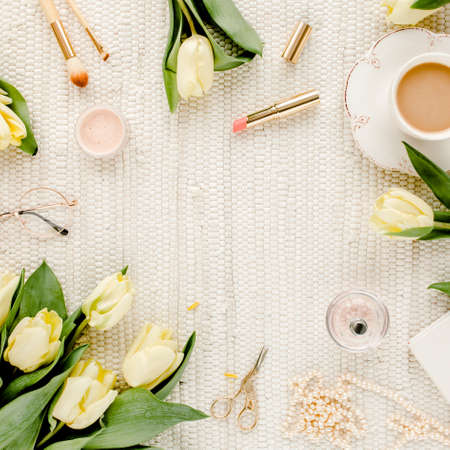Female workspace with yellow tulip flowers, womens fashion golden accessories, diary, glasses on...