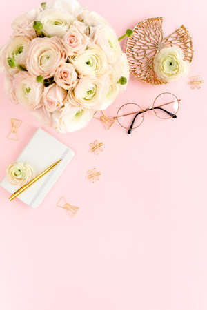Stylized, pink womens home office desk. Workspace with bouquet ranunculus and roses, clipboard on pink background. Flat lay. Top view.の写真素材