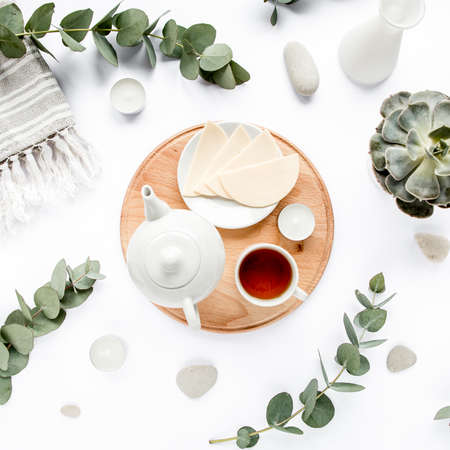 Breakfast with cheese, leaves eucalyptus, cutting board and black tea composition with on white background. Flat lay, top viewの写真素材
