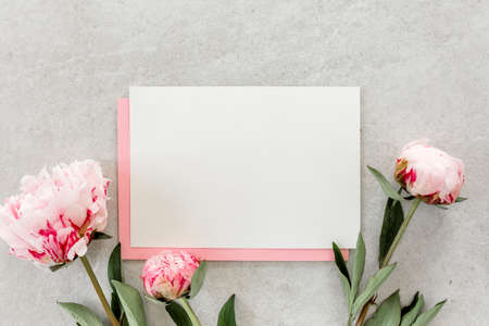 Mockup invitation, blank paper greeting card, pink envelope and peonies on gray stone table. Flower background. Flat lay, top view.の写真素材