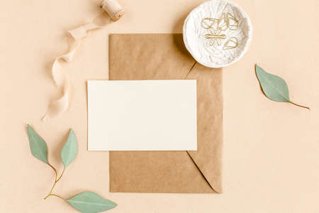 Mockup invitation, blank greeting card and craft envelope, green leaves eucalyptus. Flat lay, top view.の写真素材
