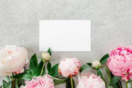 Mockup invitation, blank paper greeting card and peonies on gray stone table. Flower background. Flat lay, top view.の写真素材