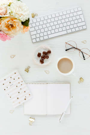Flat lay womens office desk. Female workspace with computer, pink roses flowers, accessories, golden diary, glasses on white background. Top viewの写真素材