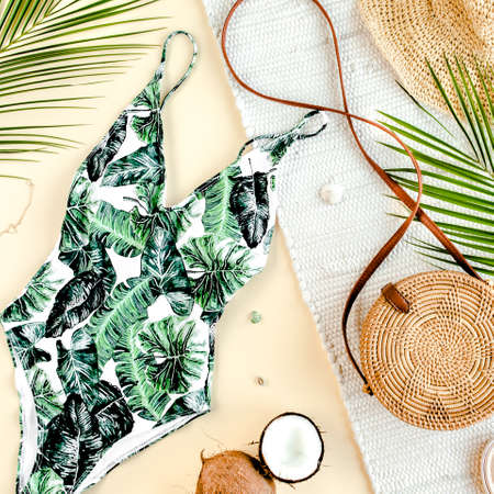Womans beach accessories: swimsuit with tropical print, rattan bag, straw hat, tropical palm leaves on yellow background. Summer background.の写真素材