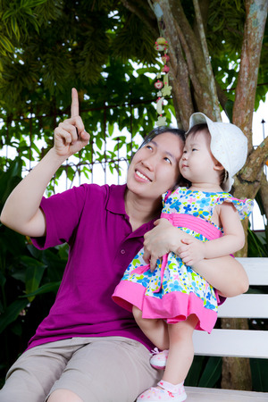 Young asian woman and cute little daughter happily in the backyard,mother pointing upの写真素材
