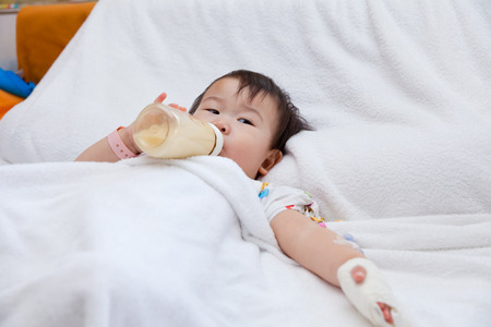 Little asian girl lying and suck up milk on a sickbed in hospital, saline intravenous (IV) on handの写真素材