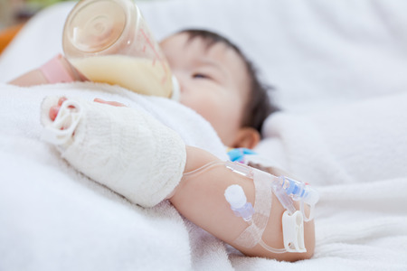 Little asian girl lying and suck up milk on a sickbed, saline intravenous (IV) on hand, shallow depth of field (DOF) saline intravenous (IV) in focus ,face out of focusの写真素材