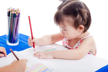 Asian girl sitting at the table and drawing by colour pencil with her friend, isolated on white backgroundの写真素材