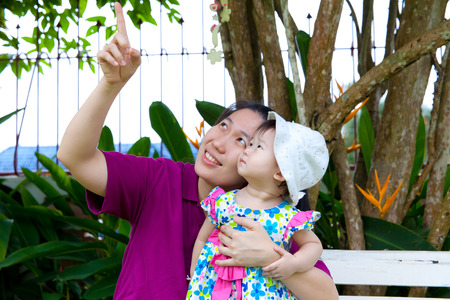 Young asian woman and cute little daughter happily in the backyard,mother pointing upの写真素材