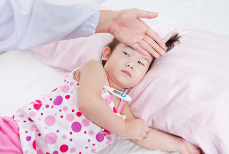 Sick little girl nursed by a pediatrician, doctor touching forehead little asian girl,girl lying with digital mercury thermometerの写真素材