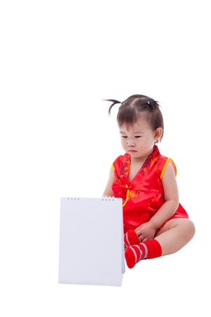 Little asian girl (thai) in traditional chinese dress, cheongsam is typical china dress, identity culture of Chinese New Year festival, child looking at blank paper desk spiral calendar, isolated on white backgroundの写真素材