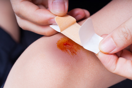 Closeup of child knee with a plaster (for wounds) and bruise, Mother provides first-aidの写真素材