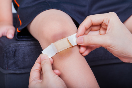 Closeup of child knee with a plaster (for wounds) and bruise, Mother provides first-aidの写真素材